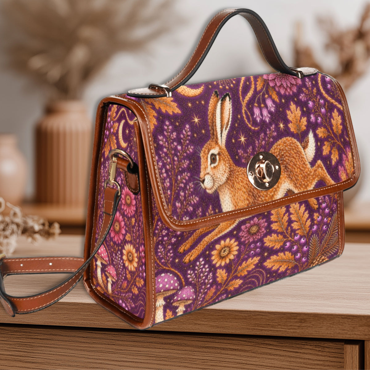 A purple handbag with a brown rabbit and floral woodland print, featuring brown leather trim and a top handle, displayed on a wooden surface.