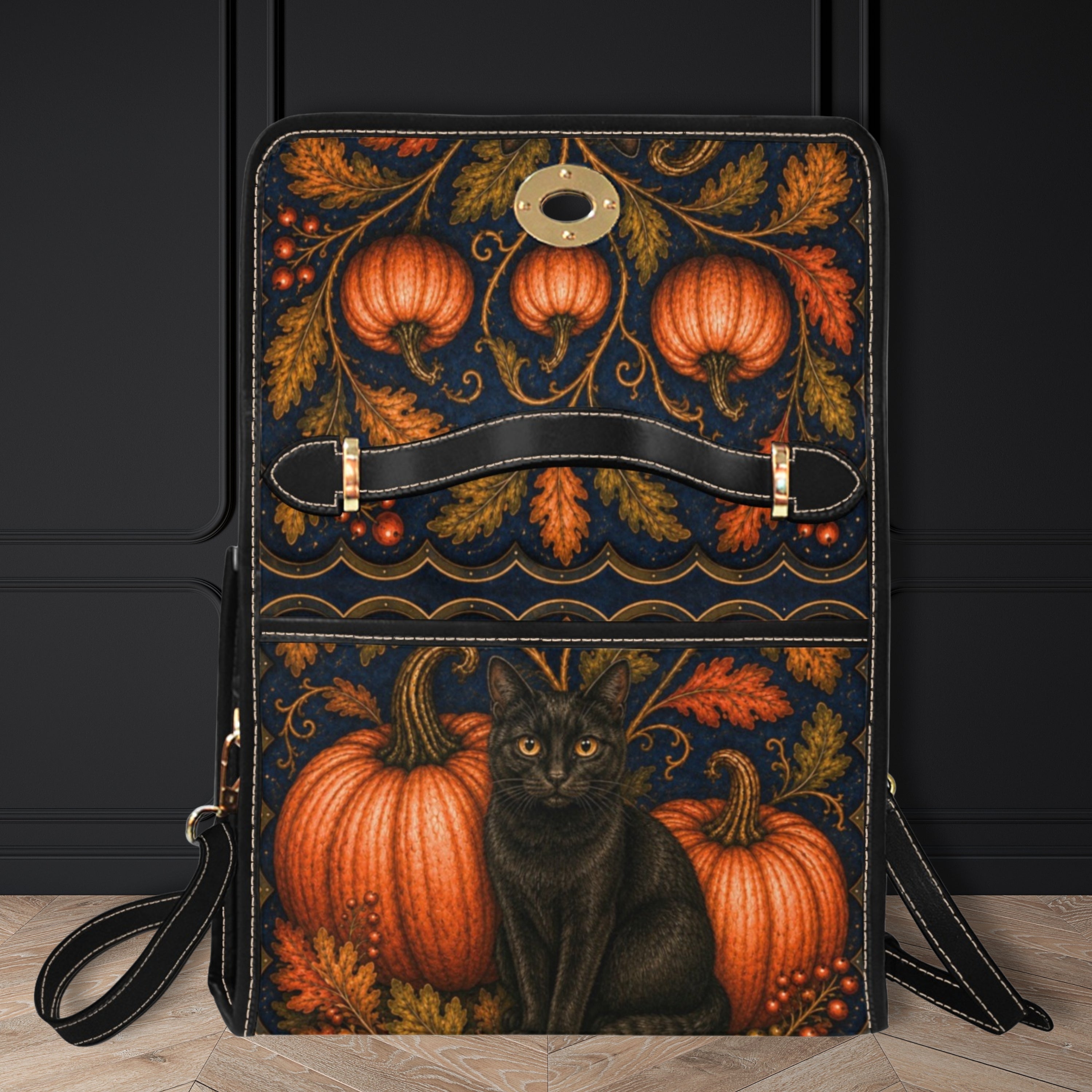 A black faux-leather crossbody bag with a decorative autumn and Halloween print featuring pumpkins, leaves, and a black cat, set against a dark paneled wall and light wood floor.