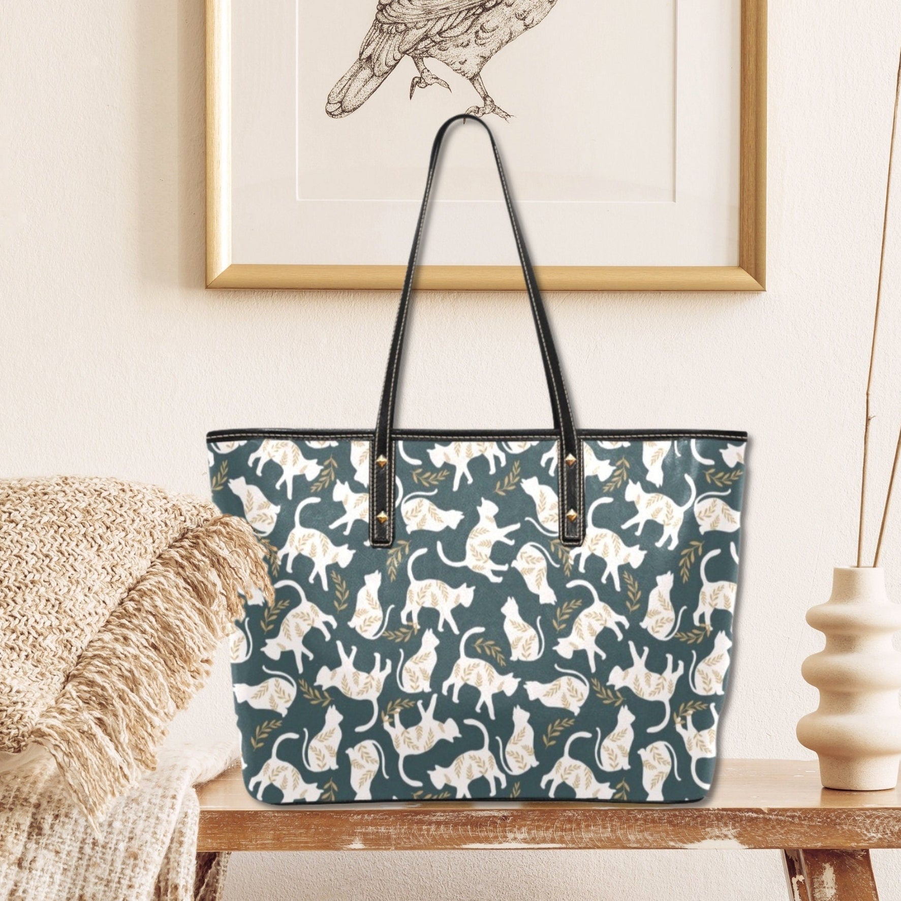 Tote bag with cat pattern on a wooden table against a neutral wall with a framed picture.