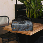 Black handbag with a cityscape design on a wooden table with a plant in the background