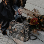 Dragon-themed handbag on a stone surface with flowers