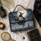A witch-themed handbag with a printed illustration of a wizard riding a broomstick under a full moon, styled in a cozy flat-lay with a 'Night Bloom' bottle, candle, mirror, necklace, and a 'Book of Shadows' on white fabric.