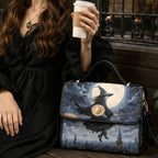 A woman in a black dress holds a white coffee cup beside a structured handbag printed with a witch riding a broomstick in front of a full moon and castle skyline.