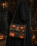 A woman in a long black dress carries a dark crossbody bag decorated with orange pumpkins, autumn leaves, and a black cat, photographed in a dimly lit Halloween-themed outdoor setting.