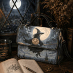 A witch-themed handbag with a printed illustration of a witch riding a broomstick in front of a full moon, styled on a wooden table with books, a candle, and dried flowers.