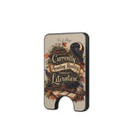 A slim black wallet card holder featuring a vintage-style illustrated cover with a raven, books, autumn leaves, and the text 'Currently Avoiding Reality Through Literature' on a light beige background.