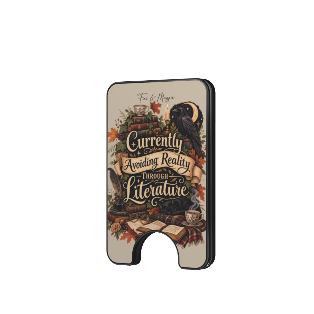 A slim black wallet card holder featuring a vintage-style illustrated cover with a raven, books, autumn leaves, and the text 'Currently Avoiding Reality Through Literature' on a light beige background.