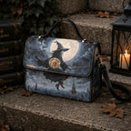 A structured handbag with a witch riding a broomstick under a full moon design, styled on stone steps next to a black lantern and old books.