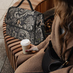 Person sitting on a bench with a patterned handbag and a coffee cup.