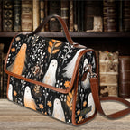 A rectangular shoulder bag with a black background and a ghost and bird pattern, featuring brown leather trim and handle, displayed on a wooden table with a blurred bookshelf background.